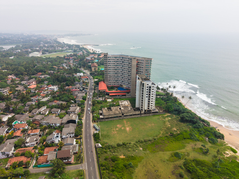 Aerial view of a modern high rise building and residential houses along the coastline with a road running parallel to the ocean in Galle Southern Province Sri Lanka. Aerial view of a modern high rise building and residential houses along the coastline with a road running parallel to the ocean in Galle Southern Province Sri Lanka.