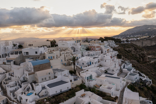 Aerial view of gleaming white architecture cascading down dramatic caldera cliffs under a sky ablaze with golden sunset rays Oia Thira Greece. Aerial view of gleaming white architecture cascading down dramatic caldera cliffs under a sky ablaze with golden sunset rays Oia Thira Greece.