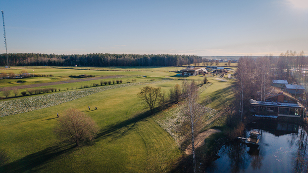 Valmiera Latvija 18 November 2025 Aerial view of a golf club building and course on a frosty morning with golfers on the green a small pond and surrounding trees.