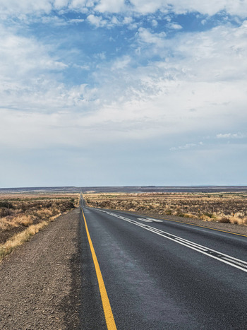 View of a long straight asphalt road stretching through the semi arid landscape of the Karoo under a blue sky with scattered clouds Beaufort West Western Cape South Africa. View of a long straight asphalt road stretching through the semi arid landscape of the Karoo under a blue sky with scattered clouds Beaufort West Western Cape South Africa.
