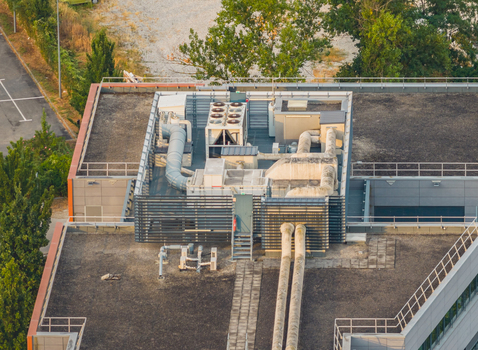 Aerial view of a modern building rooftop featuring industrial HVAC units ventilation ducts and technical equipment set against a flat roof surface in Alixan Auvergne Rhone Alpes France.
