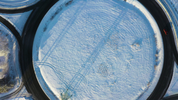 Aerial view of a snow covered circular roundabout with tire tracks and a red vehicle in Latvija. Aerial view of a snow covered circular roundabout with tire tracks and a red vehicle in Latvija.