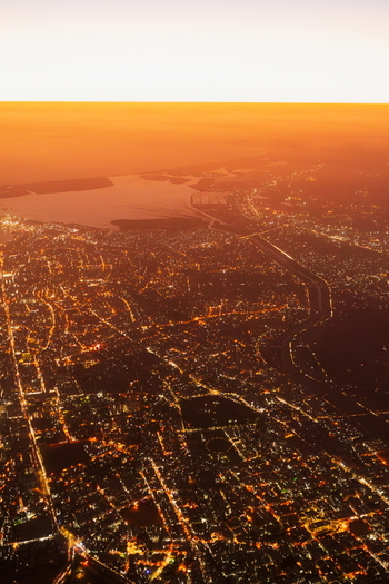 Aerial view of the sprawling city of Karachi at night with illuminated streets dense urban grid and the coastline visible under a warm sunset sky in Karachi Sindh Pakistan.