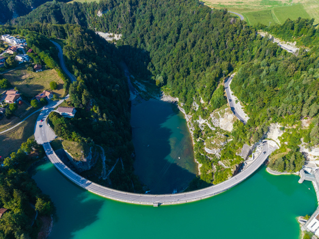 Aerial view of the Barrage de Rossens dam spanning the turquoise waters of the reservoir surrounded by dense green forests and winding roads in Pont la Ville Fribourg Switzerland.