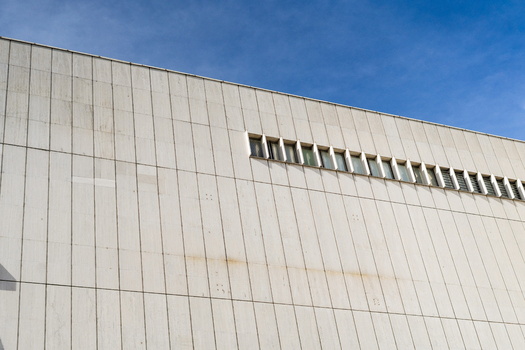 View of the minimalist white facade of a modern building with vertical stone panels and a row of narrow windows under a clear blue sky in Bratislava Bratislava Region Slovakia. View of the minimalist white facade of a modern building with vertical stone panels and a row of narrow windows under a clear blue sky in Bratislava Bratislava Region Slovakia.