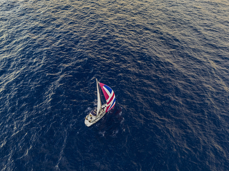 Aerial view of a sailboat with a vibrant red white and blue spinnaker sail cruising across the deep blue rippled waters of the Pacific Ocean near Waimea Hawaii United States. Aerial view of a sailboat with a vibrant red white and blue spinnaker sail cruising across the deep blue rippled waters of the Pacific Ocean near Waimea Hawaii United States.