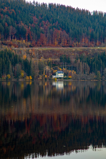 View of a solitary house on the shore of a calm lake reflecting the vibrant autumn colors of the surrounding dense forest in Breitnau Baden Wurttemberg Germany. View of a solitary house on the shore of a calm lake reflecting the vibrant autumn colors of the surrounding dense forest in Breitnau Baden Wurttemberg Germany.
