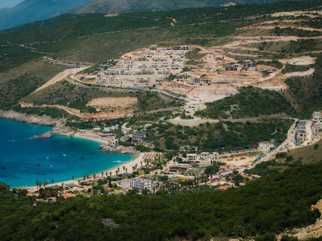 Aerial view of Aquarium Beach with turquoise water sandy shores and new construction developments on the green hillsides in Jala Vlore County Albania. Aerial view of Aquarium Beach with turquoise water sandy shores and new construction developments on the green hillsides in Jala Vlore County Albania.