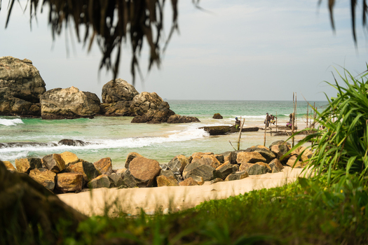 View of stilt fishermen sitting on wooden poles in the turquoise ocean near a rocky shoreline and sandy beach Koggala Southern Province Sri Lanka. View of stilt fishermen sitting on wooden poles in the turquoise ocean near a rocky shoreline and sandy beach Koggala Southern Province Sri Lanka.