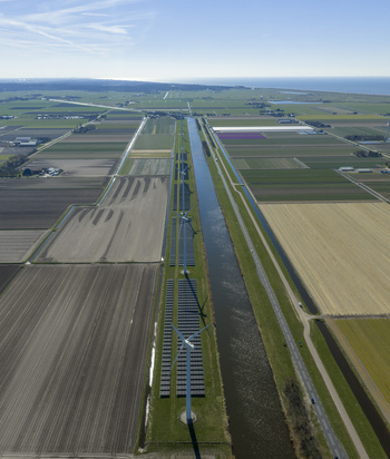 Aerial view of wind turbines and solar panels along a straight canal through agricultural fields with the sea in the distance Netherlands. Aerial view of wind turbines and solar panels along a straight canal through agricultural fields with the sea in the distance Netherlands.