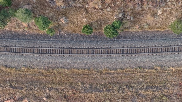 Aerial view of railroad tracks curving through a natural landscape with dry grass rocky terrain and scattered pine trees in Golden Colorado United States.
