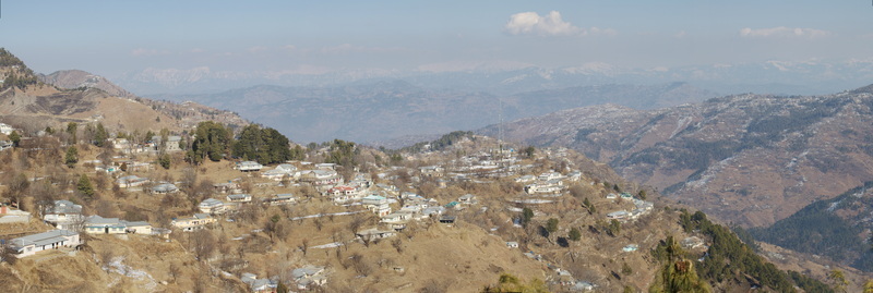 Aerial view of the panoramic landscape of Galiyat featuring scattered mountain houses terraced slopes and distant peaks under a clear sky in Galiyat Pakistan.