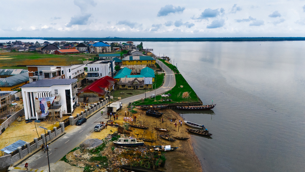 Aerial view of a coastal settlement featuring modern and traditional buildings a winding road and wooden boats moored along the riverbank in Rivers Nigeria.