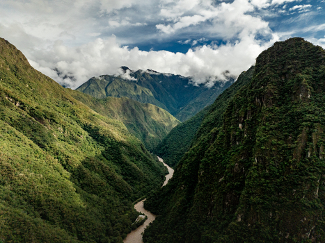 Aerial view of the Urubamba River flowing through a deep lush green mountain valley under a cloudy sky in Aguas Calientes Cusco Peru. Aerial view of the Urubamba River flowing through a deep lush green mountain valley under a cloudy sky in Aguas Calientes Cusco Peru.