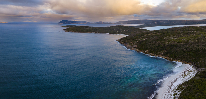 Aerial view of Quaranup Beach featuring turquoise waters sandy shores and rugged coastal cliffs under a dramatic cloudy sky in Albany Western Australia Australia.