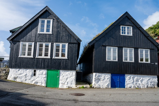 View of traditional black wooden houses with grass roofs and white stone foundations under a clear blue sky in Faroe Islands. View of traditional black wooden houses with grass roofs and white stone foundations under a clear blue sky in Faroe Islands.
