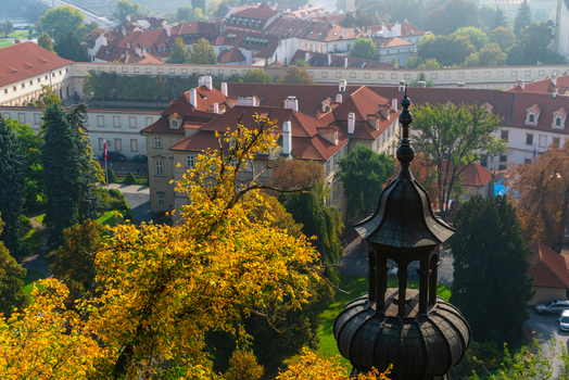 View of historic buildings with red tiled roofs and a dark church tower surrounded by autumn trees in Prague Prague Czechia.
