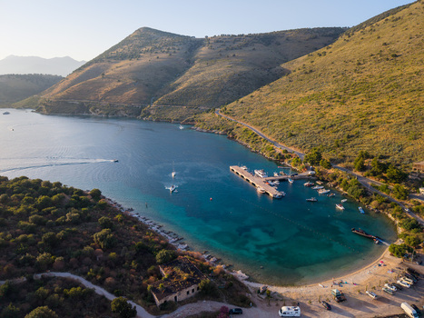 Aerial view of the turquoise waters of Porto Palermo bay with a small pier boats and a winding road along the arid hills Porto Palermo Qarku i Vlores Albania. Aerial view of the turquoise waters of Porto Palermo bay with a small pier boats and a winding road along the arid hills Porto Palermo Qarku i Vlores Albania.