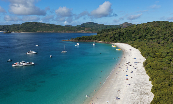 Aerial view of Whitehaven Beach with its iconic white silica sand turquoise waters and anchored boats along the lush coastline in Whitsundays Queensland Australia.