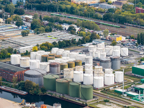 Aerial view of TanQuid Tanklager Berlin featuring large cylindrical storage tanks in white and green situated along a canal with railway tracks in Berlin Berlin Germany.