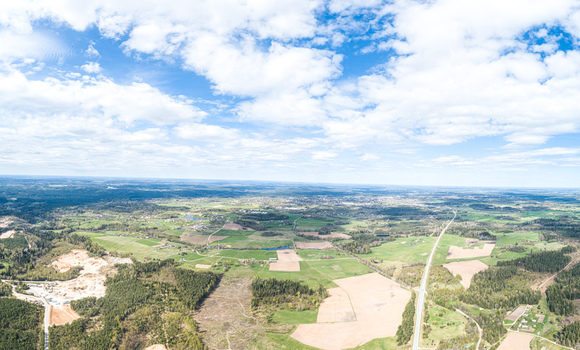 Aerial view of a rural landscape featuring green agricultural fields patches of forest and a winding road under a bright blue sky with scattered clouds in Latvia. Aerial view of a rural landscape featuring green agricultural fields patches of forest and a winding road under a bright blue sky with scattered clouds in Latvia.