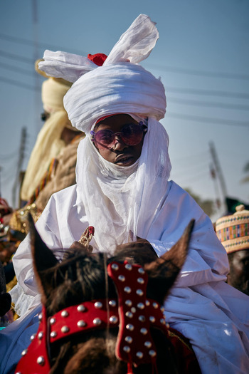 Zaria Nigerian 22 March 2026 View of a regal figure in brilliant white attire and dark shades mounted on a dark horse with striking red studded tack under a bright sky. Zaria Nigerian 22 March 2026 View of a regal figure in brilliant white attire and dark shades mounted on a dark horse with striking red studded tack under a bright sky.