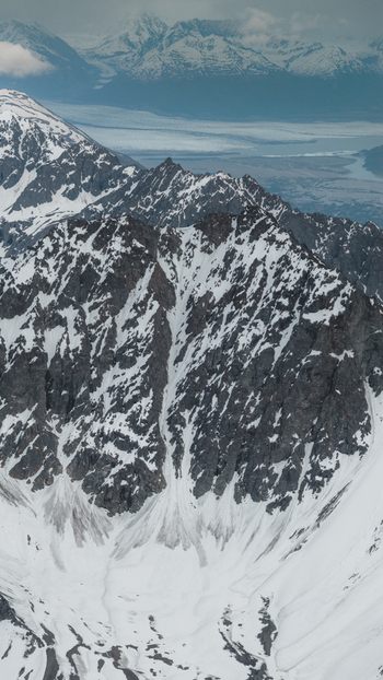 Aerial view of the rugged snow capped peaks and glaciers of the Alaska Wilderness featuring steep rocky ridges and deep valleys under a cloudy sky in Palmer Alaska United States. Aerial view of the rugged snow capped peaks and glaciers of the Alaska Wilderness featuring steep rocky ridges and deep valleys under a cloudy sky in Palmer Alaska United States.