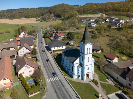 Aerial view of the light blue church of Saint Joseph with its tall spire surrounding village houses and a road winding through green hills Kriva Zilina Region Slovakia.