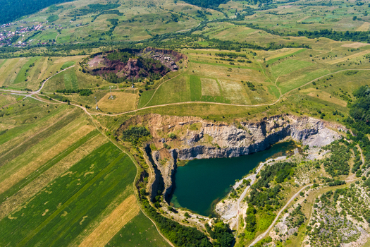 Brasov Brasov Romania 21 September 2026 Aerial view of a flooded quarry with deep blue water surrounded by lush green fields rolling hills and rural landscape. Brasov Brasov Romania 21 September 2026 Aerial view of a flooded quarry with deep blue water surrounded by lush green fields rolling hills and rural landscape.