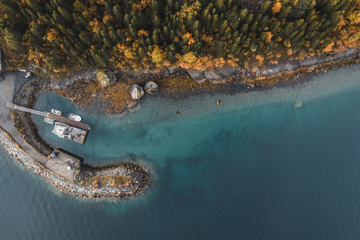 Aerial view of the Lofoten coastline featuring a small pier with boats turquoise water and dense autumn forest in Svolvaer Nordland Norway.