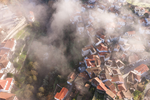 Aerial view of the historic village of Avo with its traditional red tiled rooftops partially covered by thick morning mist and surrounded by lush green vegetation in Oliveira do Hospital Coimbra District Portugal.