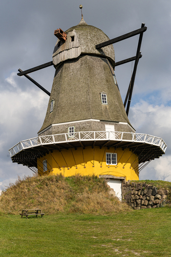 View of the historic Svanemollen windmill with its distinctive yellow base wooden shingles and surrounding grassy landscape in Kerteminde Kerteminde Municipality Denmark. View of the historic Svanemollen windmill with its distinctive yellow base wooden shingles and surrounding grassy landscape in Kerteminde Kerteminde Municipality Denmark.