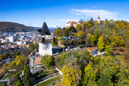 Aerial view of the Grazer Uhrturm clock tower and Schlossberg hill a blend of autumnal hues against the city skyline Graz Styria Austria.
