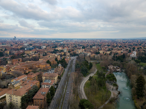 Aerial view of the urban landscape featuring red rooftops a long straight road and a park with a pond and fountains under a cloudy sky in Bologna Emilia Romagna Italy. Aerial view of the urban landscape featuring red rooftops a long straight road and a park with a pond and fountains under a cloudy sky in Bologna Emilia Romagna Italy.