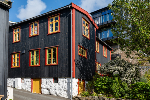 View of a traditional black wooden house with yellow window frames and a white stone foundation in the Faroe Islands. View of a traditional black wooden house with yellow window frames and a white stone foundation in the Faroe Islands.