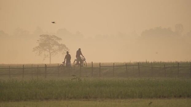View of people cycling through misty fields in Bogura Bangladesh.