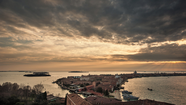 Aerial view of the historic rooftops and islands of the Venetian Lagoon under a dramatic cloudy sky with sun rays at sunset Venice Veneto Italy.