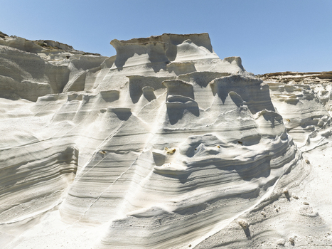Aerial view of the white volcanic rock formations of Sarakiniko Beach with smooth eroded surfaces under a clear blue sky in Milos Greece. Aerial view of the white volcanic rock formations of Sarakiniko Beach with smooth eroded surfaces under a clear blue sky in Milos Greece.