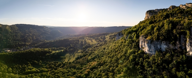 Aerial view of the Loue valley with a historic village nestled between limestone cliffs and dense green forests under a bright sun Lods Bourgogne Franche Com France.