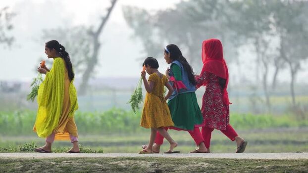 View of girls walking with carrots in a rural field Bangladesh.