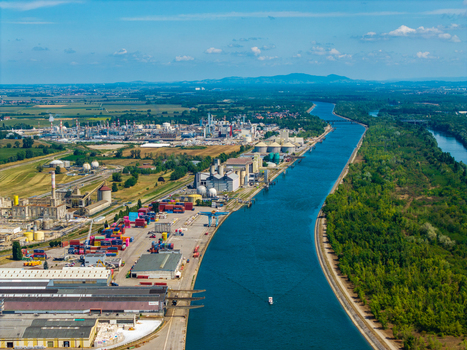 Aerial view of an industrial port area along a canal with warehouses shipping containers and a large manufacturing plant in Hombourg Grand Est France.