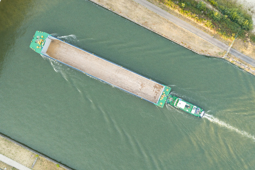 Aerial view of a cargo barge navigating the canal at Haven Genk with calm water and green banks Genk Vlaanderen Belgium.