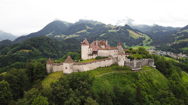Aerial view of the medieval Chateau de Gruyeres with its stone walls and towers on a green hill with the Swiss Alps and misty forests in the background Gruyeres Fribourg Switzerland.