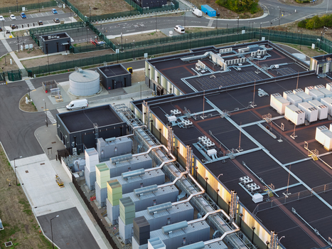 Aerial view of a modern data center facility featuring complex cooling systems HVAC units on the rooftop and surrounding perimeter fencing in the United Kingdom. Aerial view of a modern data center facility featuring complex cooling systems HVAC units on the rooftop and surrounding perimeter fencing in the United Kingdom.