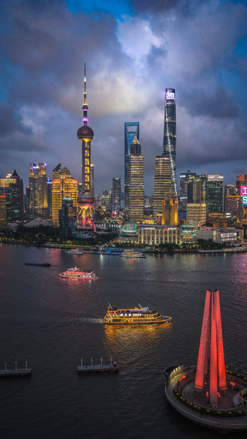 Aerial view of the illuminated Pudong skyline and The Bund with boats on the Huangpu River under a twilight sky in Shanghai Shanghai China.