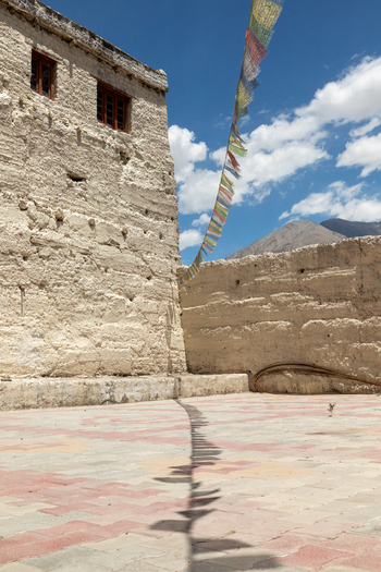View of Charasa Gonpa with colorful prayer flags hanging against a bright blue sky and textured stone walls in a paved courtyard in Charasa Ladakh India.