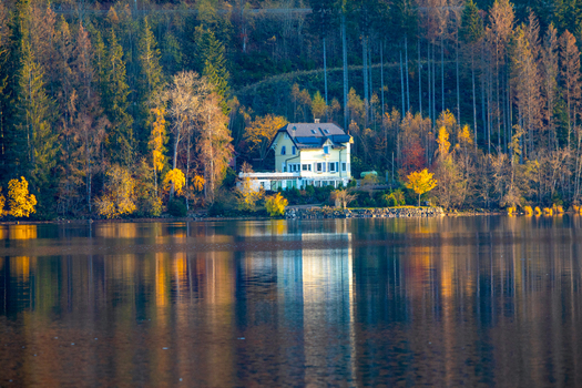 View of a house on the shore of a lake surrounded by colorful autumn forest with reflections on the water in Breitnau Baden Wurttemberg Germany. View of a house on the shore of a lake surrounded by colorful autumn forest with reflections on the water in Breitnau Baden Wurttemberg Germany.
