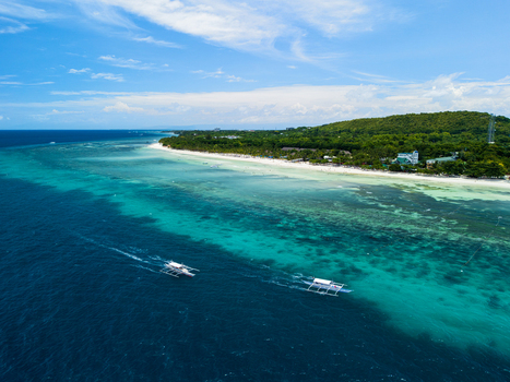 Aerial view of Dumaluan Beach with turquoise waters coral reefs and traditional outrigger boats sailing along the coast in Panglao Central Visayas Philippines.