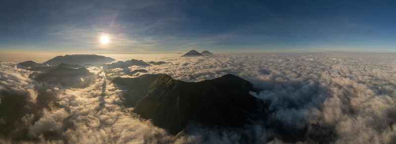 Aerial view of the mountainous landscape near Basecamp Gunung Bismo via Sikunang with green slopes rising above a sea of clouds at sunrise in Kecamatan Kejajar Jawa Tengah Indonesia.