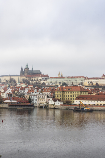 View of Prague Castle and historic red roofed buildings along the Vltava River under an overcast sky in Prague Prague Czechia. View of Prague Castle and historic red roofed buildings along the Vltava River under an overcast sky in Prague Prague Czechia.